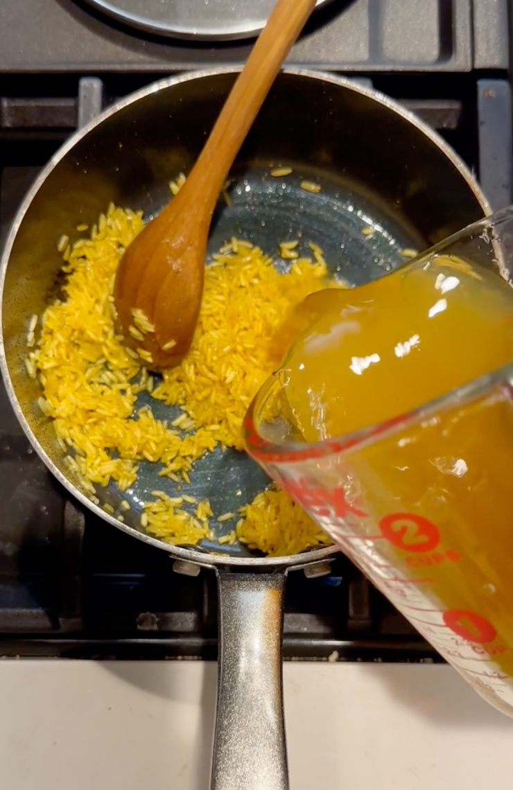 adding vegetable broth to pot with rice and spices